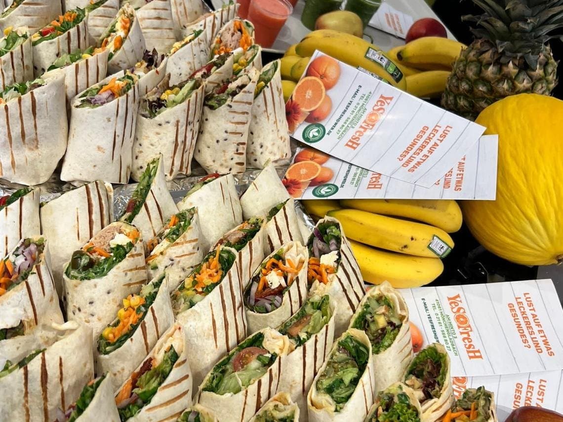 Catering-Platte mit frisch geschnittenen Wraps, Bananen, Melone und YesFresh-Flyern